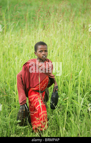 Jeune garçon Masai marcher dans l'herbe verte longue portant deux sacs en plastique Banque D'Images