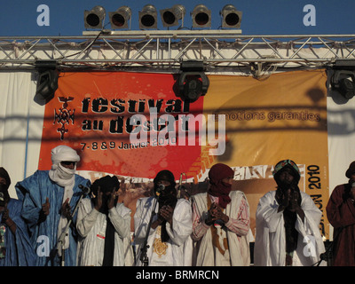 Un groupe d'hommes et femmes touareg sur la scène du Festival au Désert frappant des mains dans le cadre d'une prestation Banque D'Images