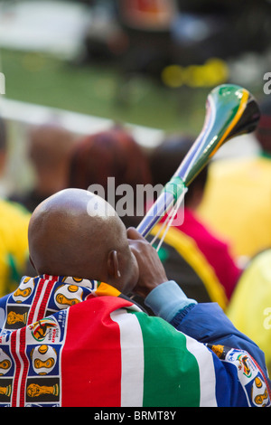 Vue arrière d'un partisan de soccer drapés dans une Coupe du Monde Afrique du Sud flag soufflant une vuvuzela lors de la coupe du monde 2010 Banque D'Images