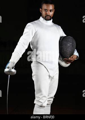 Portrait d'un tireur portant des uniformes d'escrime et de tenir une épée et un masque isolé sur fond noir Banque D'Images