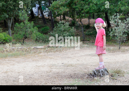 Stock photo d'une fillette de quatre ans debout sur une souche d'arbre. Banque D'Images