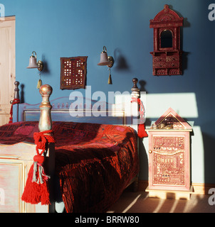Glands rouge et de velours rouge lit de style indien-couvercle sur le lit peint en bleu chambre avec table de chevet de style indien Banque D'Images