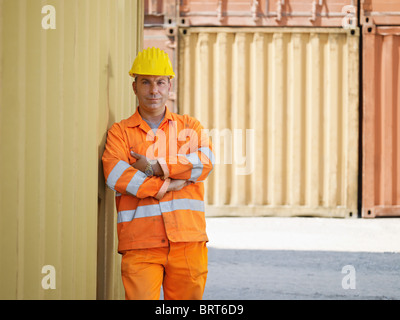 Portrait of mid adult worker standing près de conteneurs de fret et à la recherche à l'appareil photo. Vue avant, de forme horizontale, copy space Banque D'Images