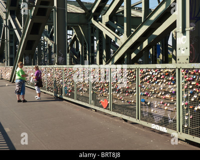 De nombreux cadenas attachés à l'Hohenzollernbrucke pont ferroviaire de Cologne, Allemagne, avec couple walking passé Banque D'Images