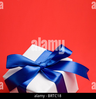 Cadeau blanc avec un ruban bleu sur fond rouge