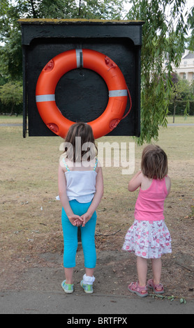 Pour les jeunes enfants debout à côté d'un orange vif vie circulaire à côté d'un lac de plaisance de courroie dans Regents Park, London, UK. Banque D'Images