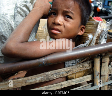 Un jeune garçon qui est un enfant travailleur est relaxant dans un panier en bois dans une rue près du marché central de Phnom Penh, Cambodge. Banque D'Images