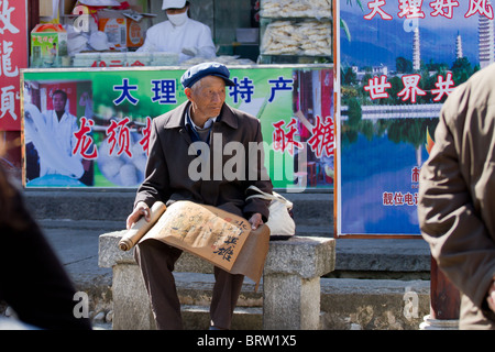 Un homme chinois âgés est assise sur un banc à Dali d'essayer de vendre son art Banque D'Images