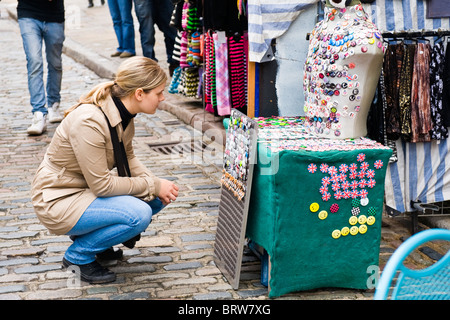 Verrouillage du marché de Camden Town , jolie jeune fille blonde en jeans et blouson de cuir s'accroupit sur l'affichage de sélection de badges nouveauté Banque D'Images