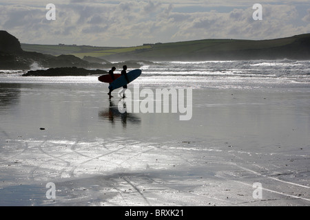 Surfers au crépuscule sur la plage de Polzeath, Cornwall, England, UK. Banque D'Images