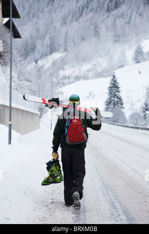 Transport skieur skis et chaussures de ski en descendant la rue des Alpes couvertes de neige en hiver à St Anton am Arlberg Tyrol Autriche Banque D'Images