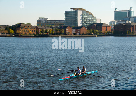 Deux personnes sculptant (aviron) sur le canal des navires de Manchester, Salford Quays, Manchester, Royaume-Uni. L'appartement Abito derrière. Banque D'Images