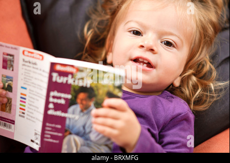 Un bébé fille de vous détendre sur un canapé-lit un livre d'étude de la langue turque. Banque D'Images