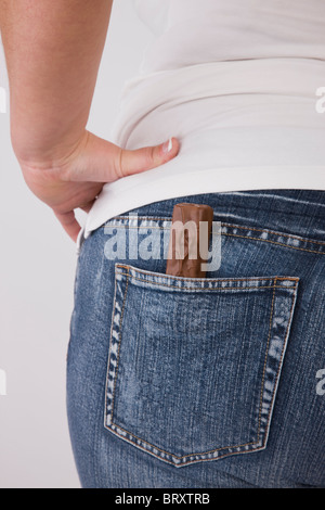 L'excès de femme avec une barre de chocolat dans la poche de jean arrière, mid section, vue arrière Banque D'Images