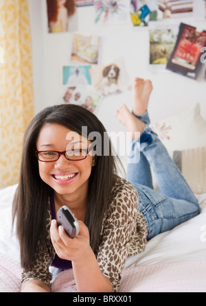 Mixed Race woman holding remote control et portant sur le lit Banque D'Images