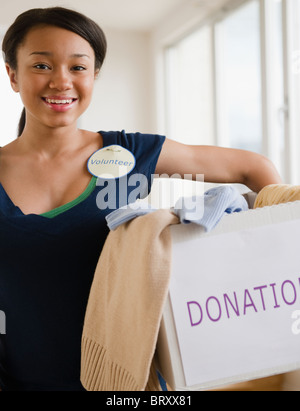 Asian teenage girl wearing 'volontaire' borne et holding box de dons Banque D'Images