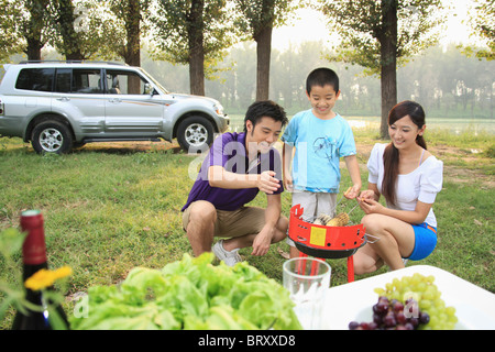 Garçon avec son parent le maïs sucré cuisson sur le barbecue Banque D'Images