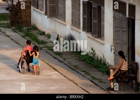 Une jeune fille pousse un homme dans un fauteuil roulant à l centre national de réadaptation à Vientiane au Laos. Banque D'Images