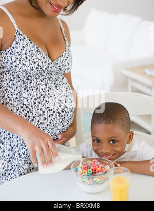 Black Boy smiling comme mère enceinte verse le lait dans les céréales Banque D'Images