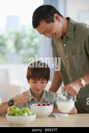 Verser le lait sur père souriant de céréales du fils Banque D'Images