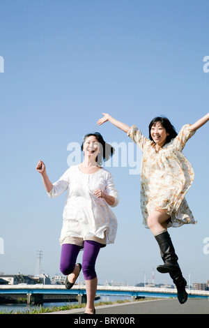 Les jeunes femmes de remorquage Jumping Under Blue Sky Banque D'Images