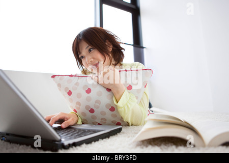 Young woman using laptop, lying on floor Banque D'Images