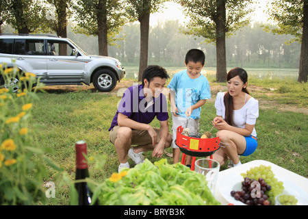 Garçon avec son parent le maïs sucré cuisson sur le barbecue Banque D'Images