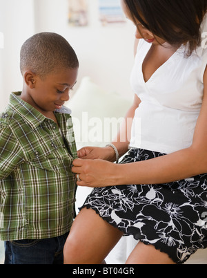 Mère noire à boutonner la chemise de son fils Banque D'Images