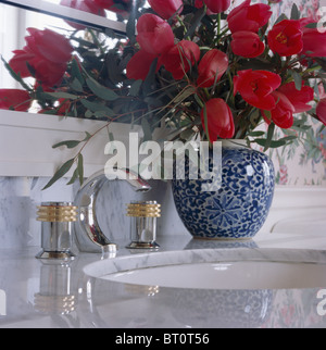 Close-up de tulipes rouges dans un vase bleu sur marbre coiffeuse avec sous-ensemble salle de bains lavabo Banque D'Images