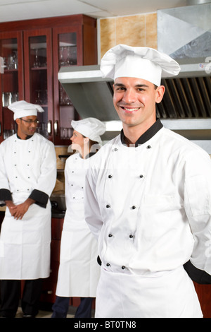 Heureux homme cuisiniers professionnels en cuisine industrielle avec des collègues derrière Banque D'Images