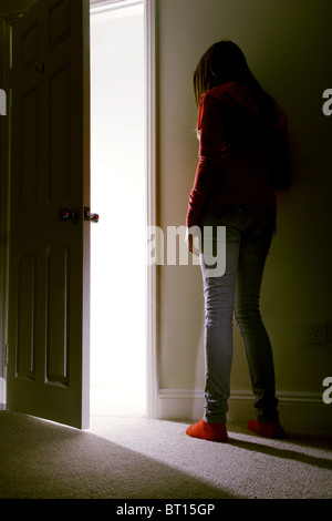 Jeune femme appuyée contre un mur de la chambre sombre comme la lumière dans les cours d'eau. Banque D'Images