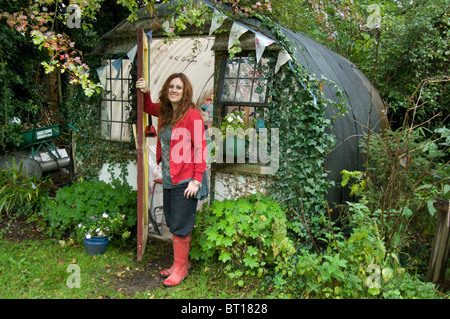 Femme en rouge bottes à la porte de son bureau et l'abri de jardin fait d'un vieux ondulée abri Banque D'Images