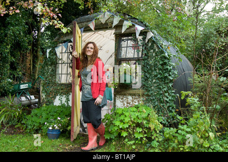 Femme en rouge bottes à la porte de son bureau et l'abri de jardin fait d'un vieux ondulée abri Banque D'Images