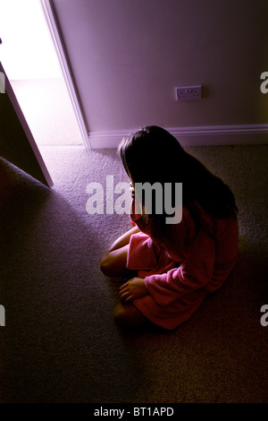 Jeune fille assise sur le plancher d'une pièce sombre en lumière le prix Banque D'Images