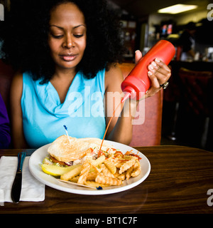 Mixed Race woman squeezing ketchup sur les frites dans diner booth Banque D'Images