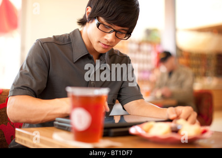 Mixed Race man using digital tablet in cafe Banque D'Images