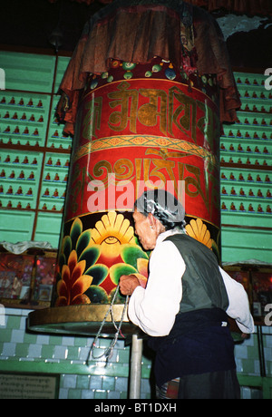 Un tibétain femme tournant un grand moulin à prières tibétain. Banque D'Images