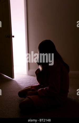 Jeune fille assise dans une pièce sombre, vue arrière porte ouverte. Banque D'Images
