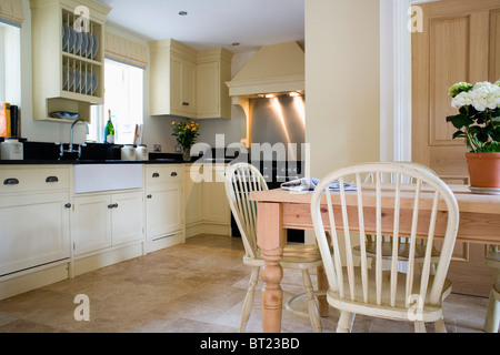 Chaises Windsor en bois pâle et table en pin dans la country traditionnelle avec cuisine équipée crème unités et un carrelage en pierre calcaire Banque D'Images