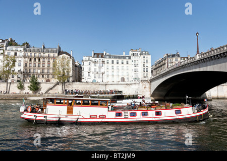 Beau vieux bateau avec quelques privilégiés à bord passe sous l'arche du Pont de la Tournelle en tandem avec un bateau d'excursion Banque D'Images