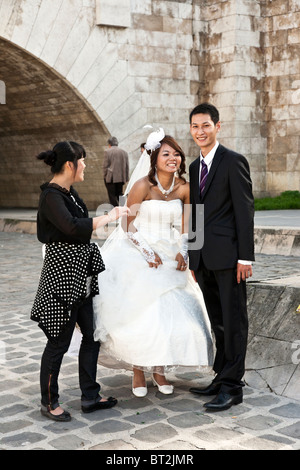 Happy smiling Asian bride & groom dans emplacement historique avec accompagnateur suite nuptiale pour préparer la séance photo Quai de la Tournelle Paris Banque D'Images