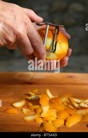 Éplucher la croûte d'une orange à la main avec un éplucheur en métal, une planche à découper en bois Banque D'Images