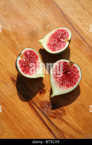 (Ficus carica) Trois figues fraîches coupées, sur une planche à découper en bois, à l'extérieur. Banque D'Images