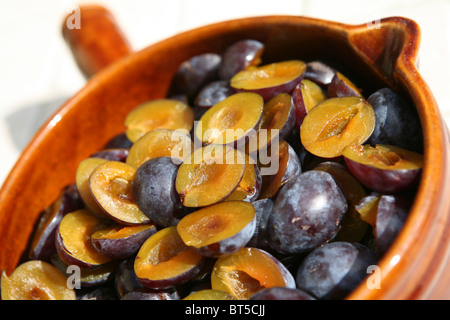 (Prunus domestica subsp. Insititia) Damsons mûrs frais, coupés en deux et délaqués, dans une casserole en céramique brune, en préparation pour la confiture de damson Banque D'Images