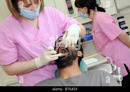 Une femme dentiste d'effectuer un contrôle dentaire sur un patient de sexe masculin avec une infirmière dentaire dans l'arrière-plan Banque D'Images