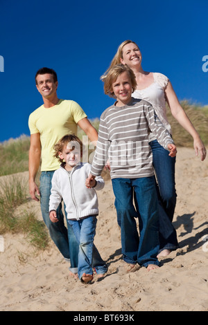 Une famille heureuse de la mère, le père et les deux fils, marcher main dans la main et s'amuser dans les dunes de sable d'une plage ensoleillée Banque D'Images