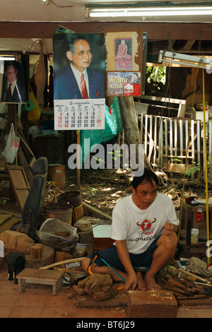 Graveur sur bois de teck bois teck coupe homme. Le Roi thaïlandais holding affiche l'arrière-plan. Bangkok, Thaïlande, septembre 2010 Banque D'Images