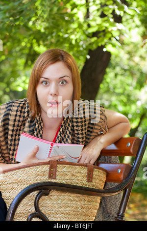 Belle femme aux cheveux rouges et à la surprise de lire sur un banc Banque D'Images