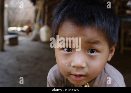 Un jeune garçon de 5 ans Karen Paduang jeune garçon réfugié joue sous sa maison en bois dans un camp de réfugiés dans le nord de la Thaïlande. Banque D'Images