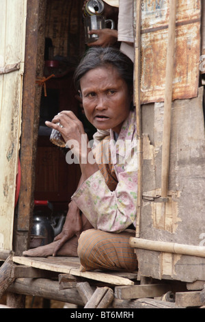 Une femme asiatique vivant dans la pauvreté est de boire une boisson alcoolisée alors qu'il était assis dans une baraque au Cambodge. Banque D'Images